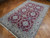 Angled view of hand-knotted Nain rug, burgundy field with pale blue and ivory rosette cartouches