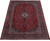 8'8" x 12'6" Persian Kashan rug angled to show deep red field and navy borders