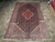 Light red and navy Kurdish Koliai wool rug laid on stone tile showroom floor