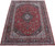 Angled full view of the 9x12 red Kashan rug showing navy border and ivory guard stripes