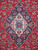 Close-up of ivory and navy lobed medallion surrounded by light blue rosettes on crimson wool field