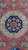 Close-up of navy central medallion with ivory arabesque halo against coral red wool field