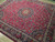 Angled view of red wool Mashad rug showing ivory guard bands and navy paisley border