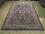 Angled showroom view showing coral salmon border, navy field and ivory fringe on hand-knotted wool rug
