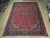 Dark pink and navy 10x13 area rug displayed on light wood showroom floor beside rolled rugs