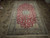 Angled showroom view of red wool and silk Nain rug with ivory palmette border