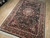 Angled view of black field 6x9 area rug with wine burgundy border and cotton fringe