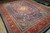 Angled floor view highlighting deep navy pile, teal accents and wide rust red main border