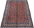 Angled display of coral red Sarouk area rug showing ivory border and blue guard stripes
