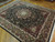 8x10 black and burgundy Oriental rug photographed at an angle on hardwood, showing silk sheen