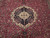 Close-up of the black and ivory lobed central medallion surrounded by fine floral vinework on burgundy wool