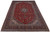 Hand-knotted 10x14 Kashan rug photographed at an angle showing dense red field and ivory fringe