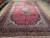 Angled view of the red and navy hand-knotted Kashan rug showing full 10x14 floral field