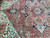 Pile detail under cool light showing olive, sage and ivory accents across the coral-red Heriz field