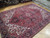 Angled view of large 8x12 wool Persian rug with ivory corner spandrels and raspberry field