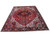 9x12 Persian Heriz rug angled on white, brick red field framed by jet black floral border