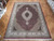 Hand-knotted wool and silk rug displayed on parquet floor showing full burgundy field and ivory borders