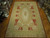 Oversize floral rug photographed on parquet showroom floor showing sage green border and terracotta corner panels