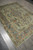 Angled view showing floral sprays and scrolling rust vine border on the green wool rug