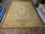 Oversize Aubusson rug laid flat on a warehouse floor beside rolled inventory, showing full ivory field