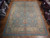 11' x 14'8" Turkish Oushak rug displayed flat on parquet showroom flooring beside stacked rugs