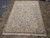Angled view of cream and light blue Tabriz rug showing silk highlights, pink bouquets and white fringe