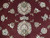 Close-up of ivory palmettes, sage green leaves and blush rosettes woven across the deep burgundy field