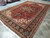 Large 8x12 Persian Heriz rug angled across tile floor, antique red and navy palette