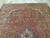 Angled view of the terracotta red field, blue palmettes and ivory spandrels filling the 9x12 rug