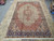 Ivory and brick red Moud rug laid flat on stone floor showing navy palmette border