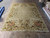 Ivory needlepoint area rug on a warehouse floor, grape clusters and floral border framing the field