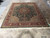 Hand-knotted Tabriz design rug displayed flat on tile showroom floor showing ivory fringe and green field