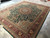 Full rug at an angle on tile floor, emerald field framed by burgundy main border