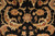 Macro detail of gold palmettes and curling serrated leaves woven in soft wool on black