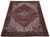 8x11 Persian Heriz rug photographed at an angle, brick red field with ivory corner spandrels