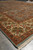 Angled corner view of blue field meeting ivory floral border on a grey tile floor