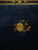 Detail of gold vase on a slender stand with leafy sprays against midnight blue wool pile