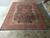 Large 1980s Persian Kashmar rug displayed on showroom tile floor beside a rolled hand-knotted rug