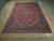 Angled showroom view of the 10x14 red Tabriz rug showing navy floral border and ivory guards