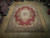 8'10" x 12' needlepoint Aubusson rug displayed on light wood showroom floor with rose garlands