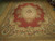 9x12 Aubusson needlepoint rug photographed at an angle, rust red field and ivory rose border