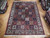 8'4 x 11'7 Bakhtiari rug displayed on parquet showroom floor among rolled Persian rugs