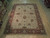Angled view of beige traditional area rug showing all over floral vines and red guard borders
