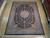 9' x 12'3" Indian Oriental rug displayed on light wood showroom floor beside rolled rug stock