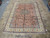 8' x 11'5" Persian rug displayed on showroom tile floor showing coral field and ivory border