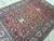 Angled view of magenta and gold floral vinework across the navy field of this hand-knotted wool rug