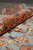 Rolled edge showing pile depth, coral border wool and green leaf accents in raking light
