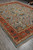 Full rug displayed at an angle in the warehouse, sky blue ground and terracotta frame