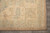Corner view of the ivory border, sage guard bands and hand-tied fringe on grey tile