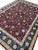 Angled view showing dense hand-knotted pile, wine red field and wide navy floral border
